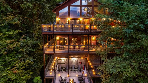 A multi-level wooden cabin with a balcony, surrounded by dense forest.