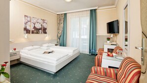 Une chambre d’hôtel avec un lit, un canapé, une télévision et une fenêtre avec des rideaux.