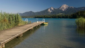 Une jetée en bois s’avance sur un lac paisible aux eaux claires, entourée d’une végétation luxuriante et avec des montagnes en arrière-plan.