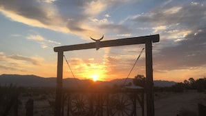 Een landelijke poort met een schedel bovenop, voor een zonsondergang met bergen op de achtergrond.