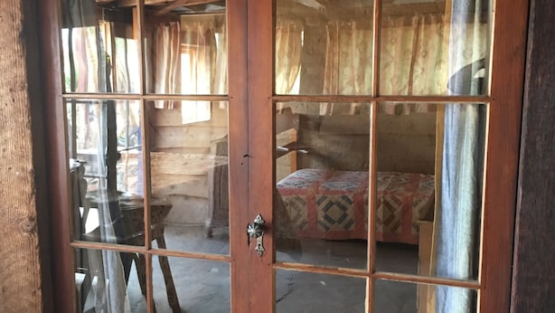 Een houten deur met ruitpanelen, een metalen handvat en een zichtbaar interieur met een bed en gordijnen.