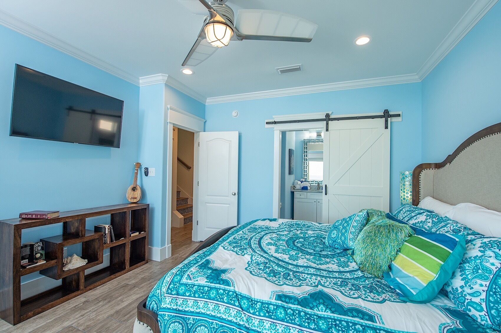 A bedroom with a bed, a TV, a wooden shelf, and a ceiling fan.