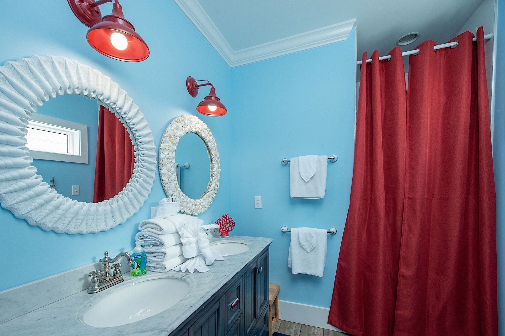 A bathroom with a blue wall, two large mirrors, a red shower curtain, and a white sink with a marble countertop.