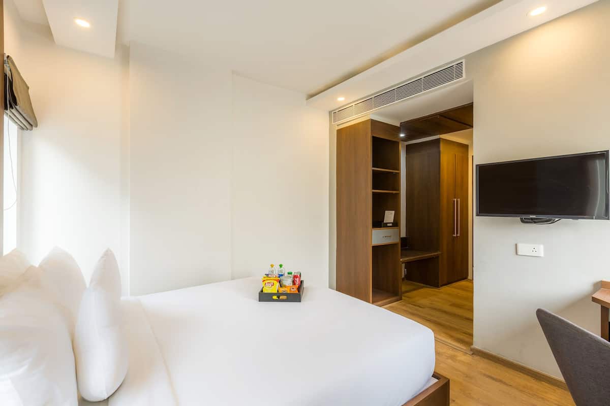 Una habitación de hotel con cama, televisión montada en la pared, armario y una mesita.