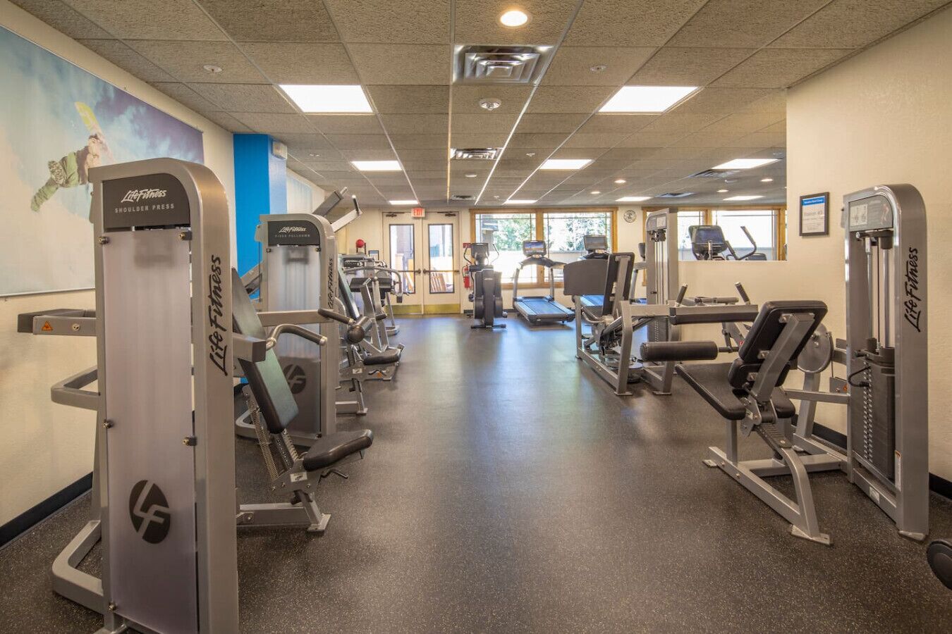 A gym with various exercise machines, a treadmill, and a wall with a poster.