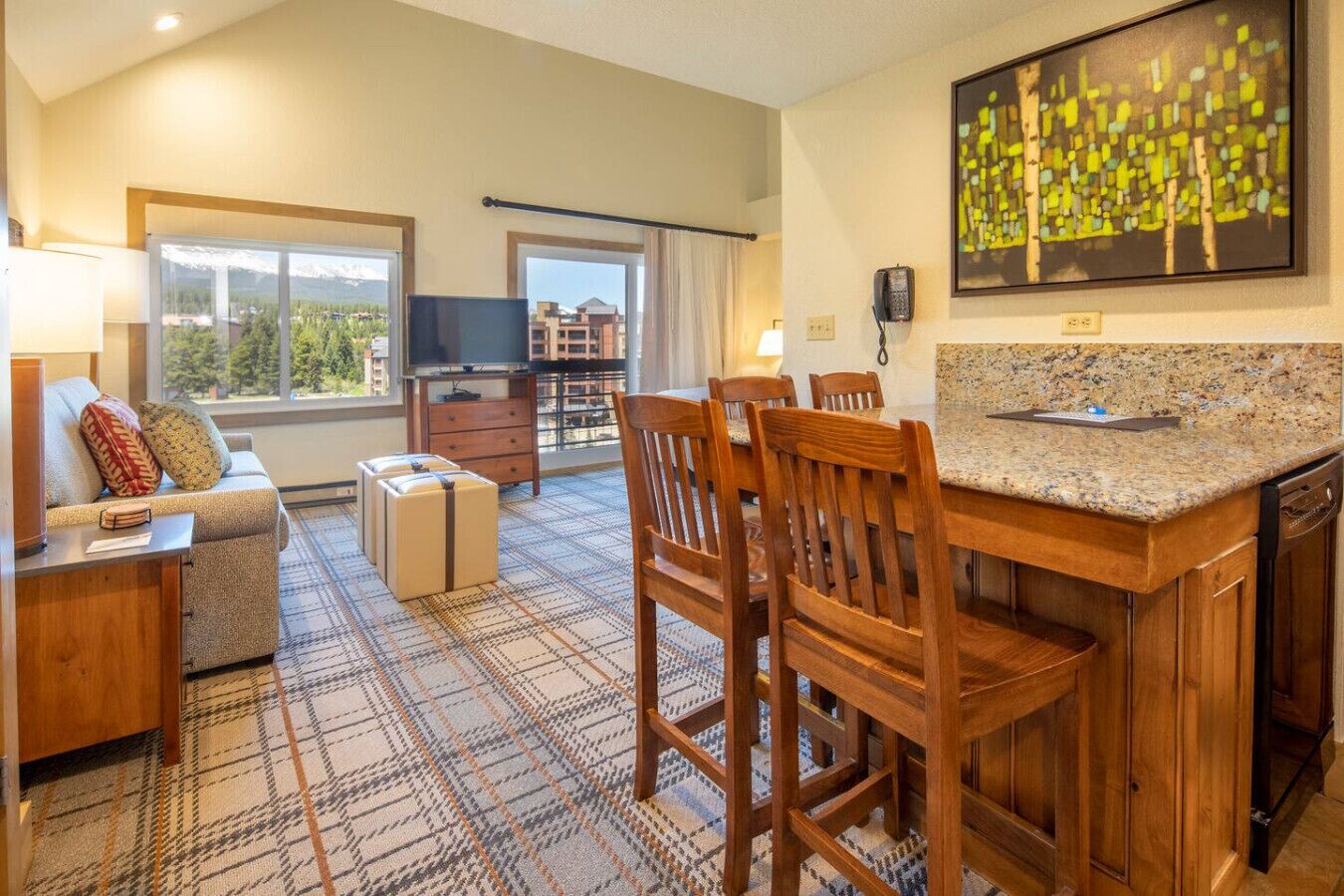 A modern hotel room with a kitchen area, a dining table, and a sofa.