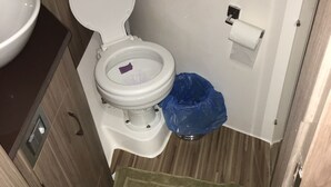 A compact bathroom with a toilet, a sink, and a blue trash bin.