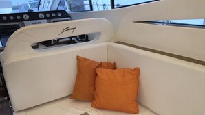 A boat interior with a white cushioned bench, two orange pillows, and a SIMRAD navigation system.