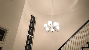 Un escalier avec des balustres blanches et une main courante noire, menant à un palier sur lequel se trouve un lustre.