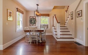 A dining area with a wooden table and chairs, a chandelier, and a staircase with white railings.