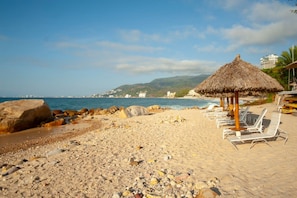 Ein Strand mit einem Reetdachschirm und Liegestühlen.