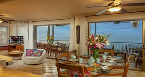 A dining area with a table set for four, a television, and a balcony with a view of the sea. - Ocean Front/Heated Pool, 6 Adults+ 2 kids under 12 (Puerto Vallarta)