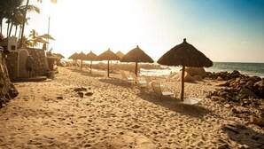 Une plage avec des parasols en chaume, des chaises longues et un mur de pierre.
