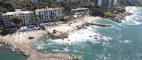 A coastal resort with multiple buildings, a sandy beach, and a rocky shoreline.