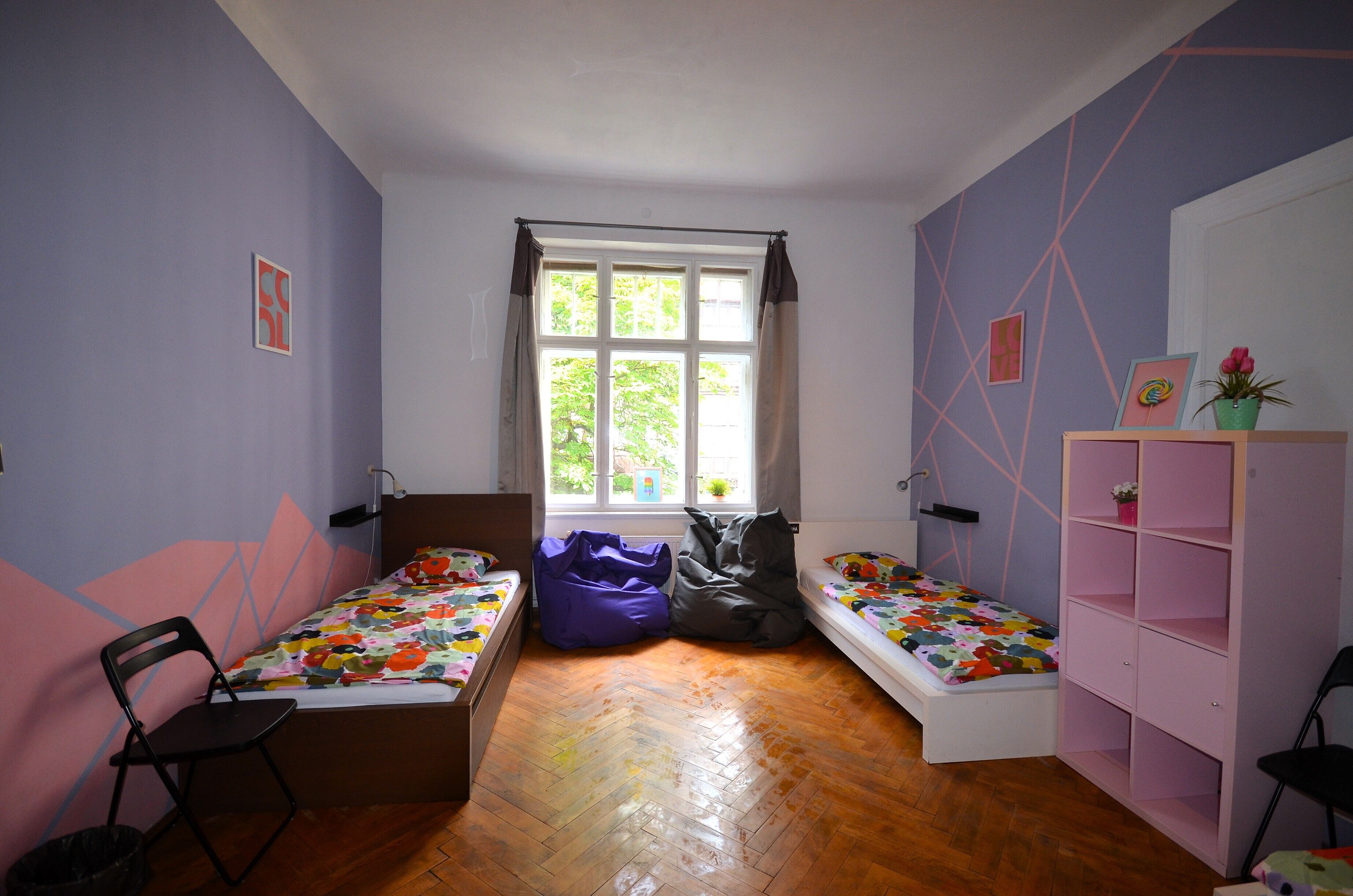 A room with two single beds, a window, a desk, and a chair.