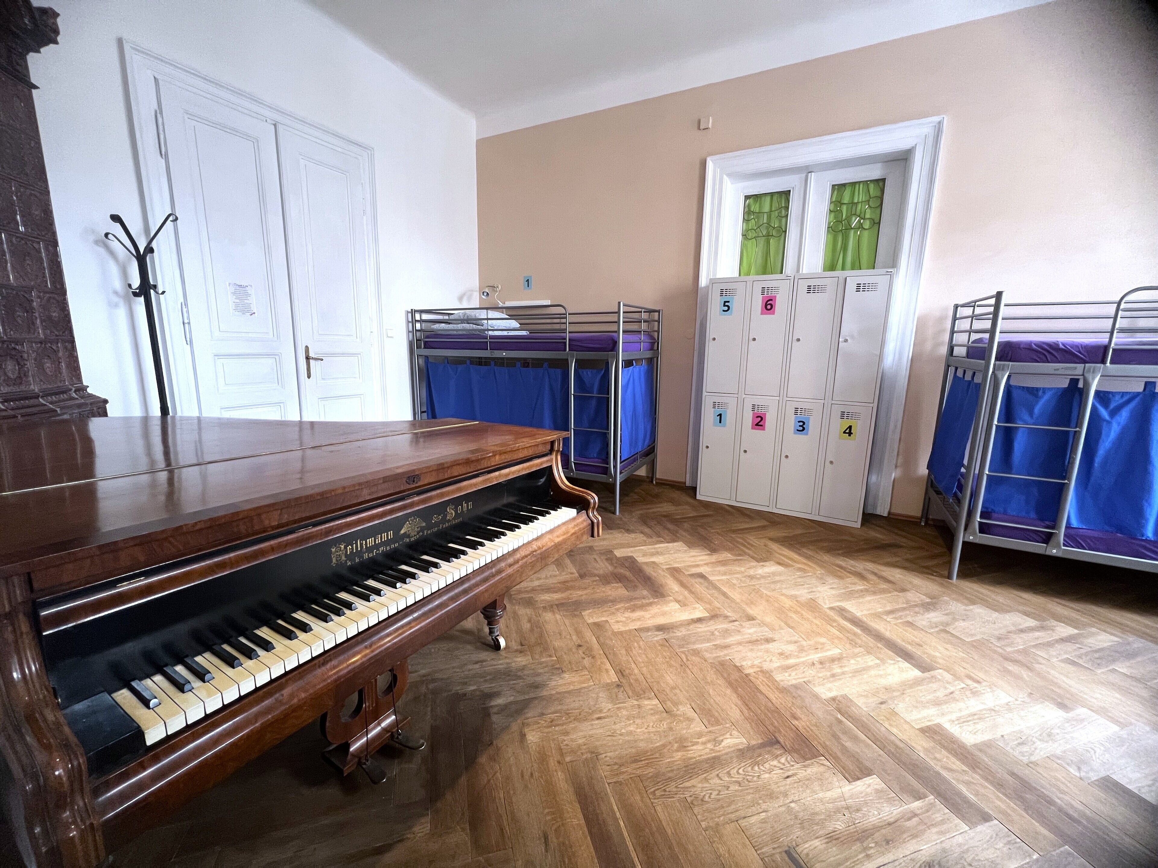 Een kamer met een vleugelpiano, stapelbedden en een aantal kluisjes.