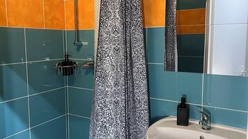 A bathroom with blue and orange tiles, a white sink, a black soap dispenser, and a shower curtain with a black and white pattern.