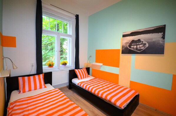 Ein Schlafzimmer mit zwei Betten, einem Fenster mit Vorhängen, einem Bild an der Wand und einer Pflanze auf der Fensterbank.