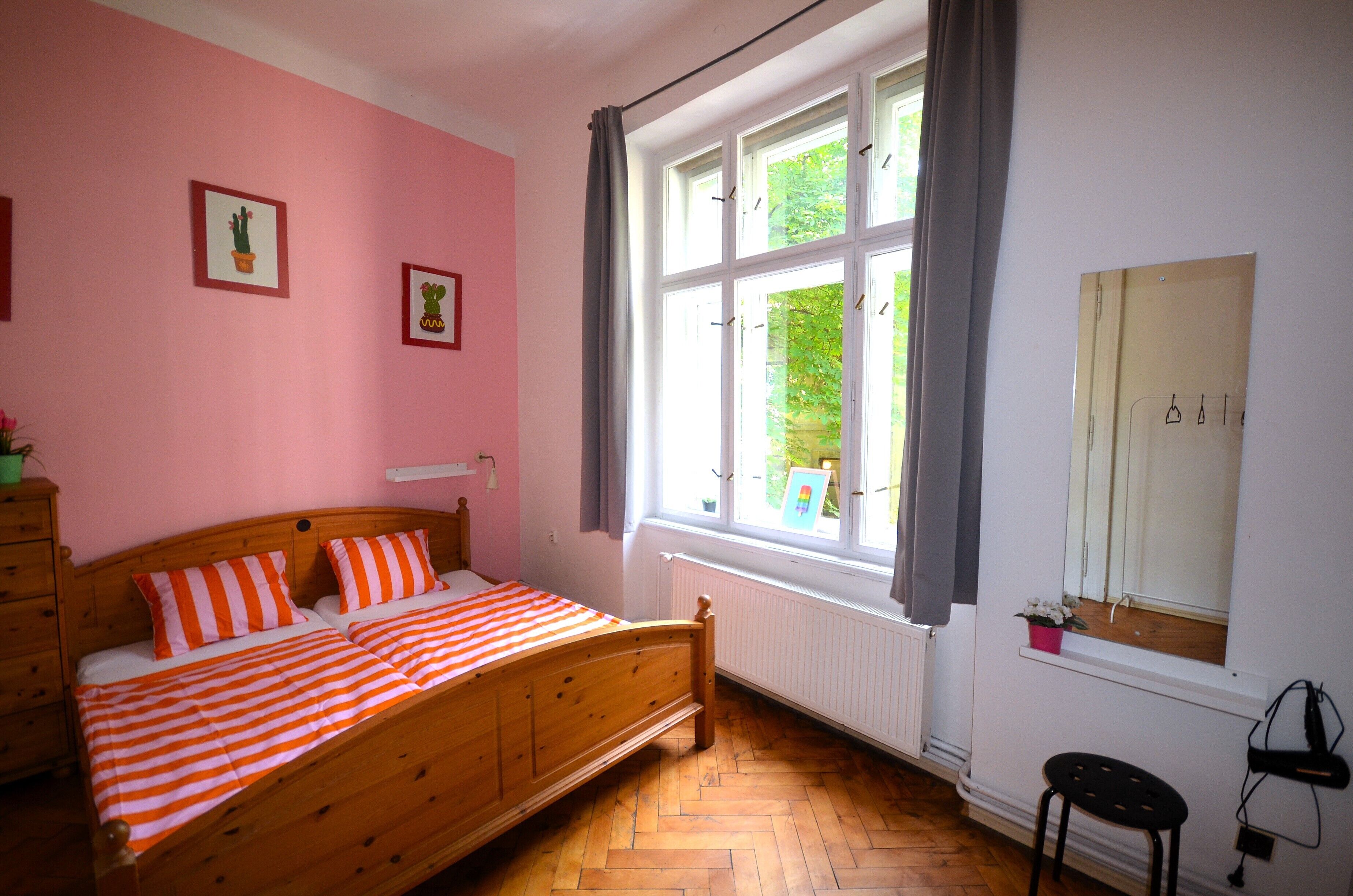 A bedroom with a wooden bed, pink walls, and a large window with curtains.