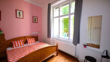 A bedroom with a wooden bed, pink walls, and a large window with curtains.