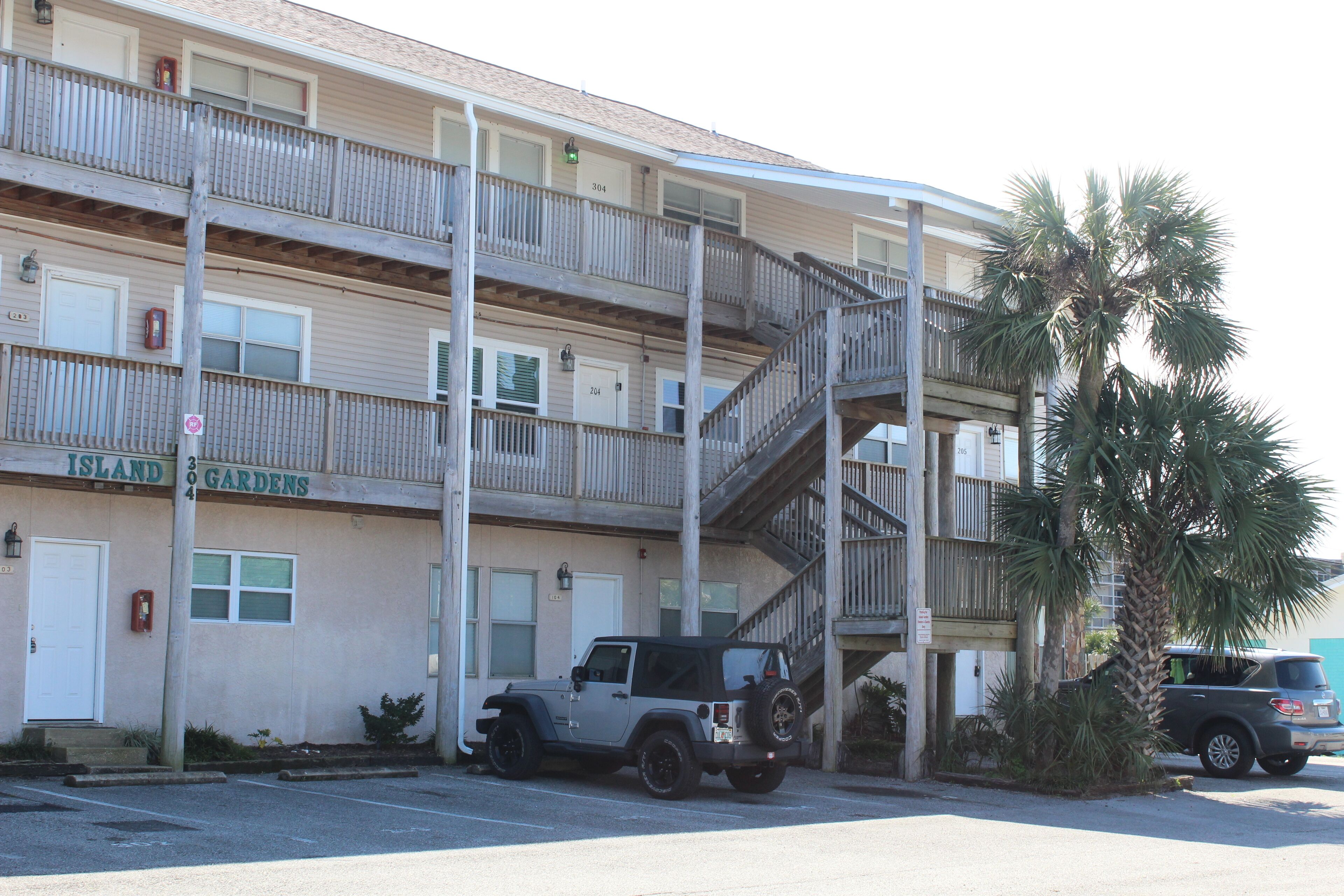Un edificio de varios pisos con balcones, un estacionamiento y una palmera.