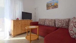 A living room with a wooden cabinet, a television, a red sofa, and a small round table. - Apartment Klara 1 on the ground floor (Krk)