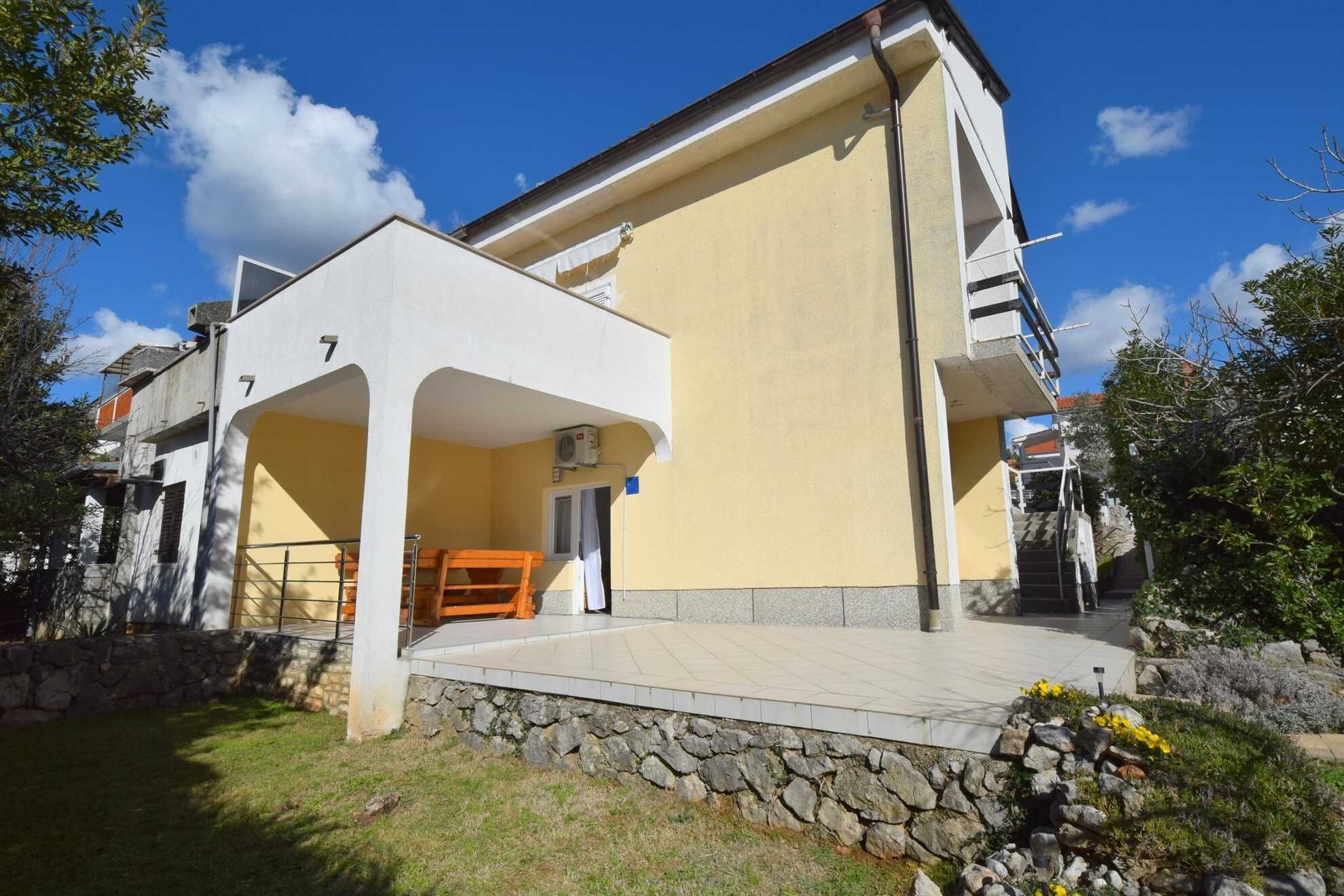 A two-story building with a balcony, stone wall, and a small garden area.
