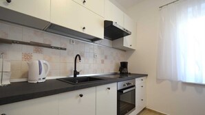 A modern kitchen with white cabinets, a black countertop, a built-in oven, a coffee maker, and a window with sheer curtains. - Apartment Klara 1 on the ground floor (Krk)
