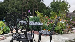 Un patio jardín con dos sillas metálicas decoradas y una pequeña mesa redonda.