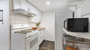 Una cocina moderna con gabinetes blancos, una campana extractora de acero inoxidable, un microondas integrado y un refrigerador de acero inoxidable.