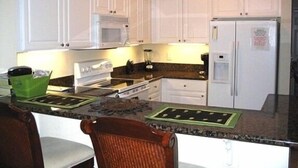 Une cuisine avec des meubles blancs, un four à micro-ondes, un réfrigérateur, une cuisinière et un coin repas comprenant une chaise et une table.