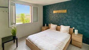 A bedroom with a large bed, two bedside tables, a window with a view of greenery, and a wall-mounted sign. - 3 bedroom cozy home in Quarante (Quarante)