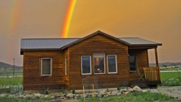 Une cabane en bois avec un toit en pente, une véranda à l’avant et un petit espace de porche.