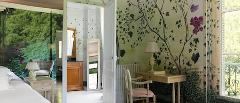A bedroom with a large window, a wooden dresser, a chair, and a nightstand.