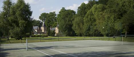 An outdoor tennis court with a net, surrounded by trees and a building in the background.