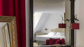 Quarto de hotel com cama, poltrona, mesa de cabeceira e espelho refletindo o ambiente.