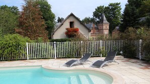 Una piscina amb dues gandules, una tanca blanca i un edifici amb una torre al fons.