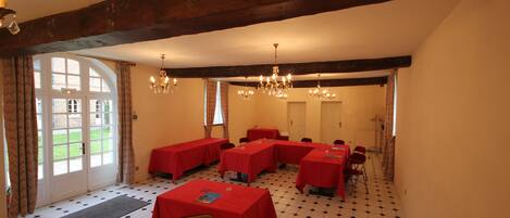 A conference room with multiple tables covered in red tablecloths, a chandelier, and a checkered floor.