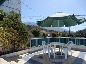 Une terrasse avec une table et des chaises sous un parasol vert, entourée d’une clôture blanche et offrant une vue sur les montagnes.