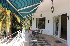 Une terrasse couverte avec un sol à carreaux, une table entourée de chaises et une lanterne suspendue.