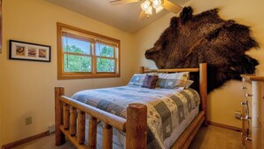 Een slaapkamer met een houten bed, een groot bont tapijt, een raam met zonwering en een plafondventilator.