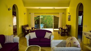 A bright yellow room with a purple sofa, wicker chairs, and a view through a glass door.