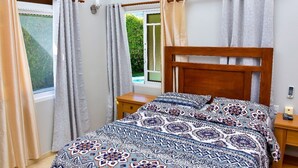 A bedroom with a wooden headboard, a patterned bedspread, and curtains on the windows.