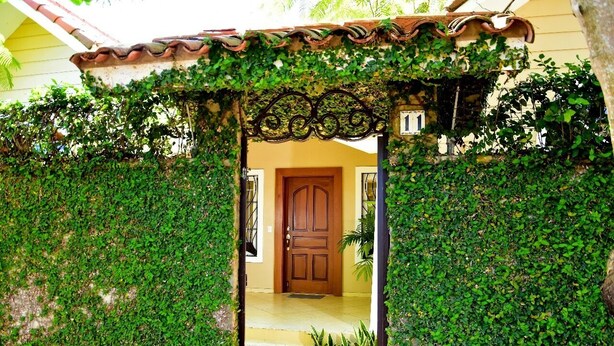 A covered entrance with a wooden door, surrounded by lush greenery.