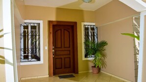 A hallway with a wooden door, a potted plant, and a window with metal bars.