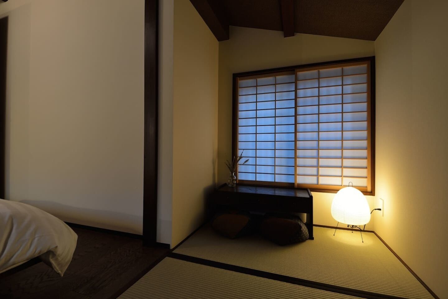 A traditional Japanese room with tatami flooring, a low wooden desk, a shoji screen window, and a bedside lamp.