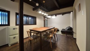 A dining area with a wooden table and chairs, a white refrigerator, and a sofa. - TAKEYA Gojo East  (竹屋五条東館) (Kyoto)