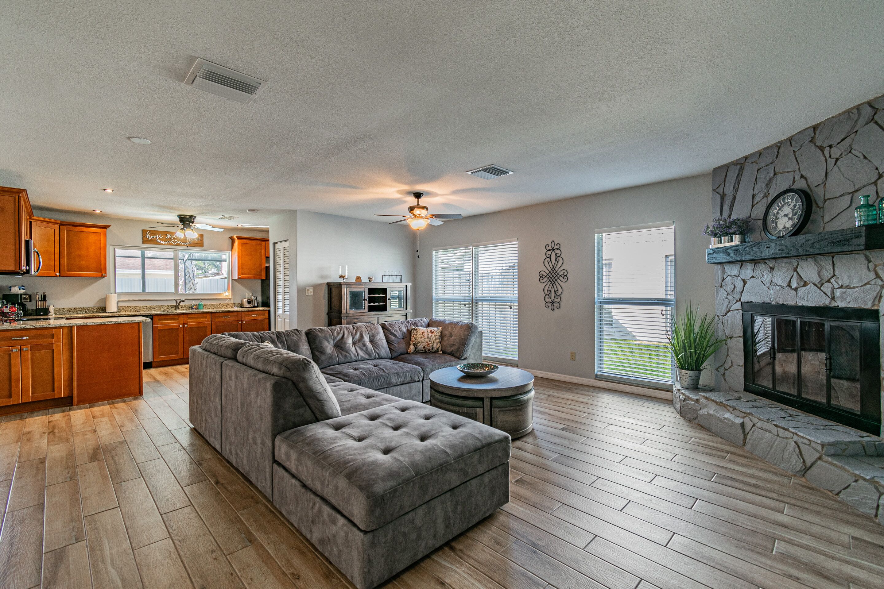 A spacious living room with a sectional sofa, a fireplace, and a kitchen area in the background.