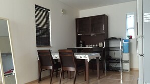 Una pequeña cocina con una mesa y sillas, una ventana con persianas, un armario empotrado y un refrigerador.