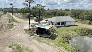 A white house with a metal roof, a dirt road, and a pond.